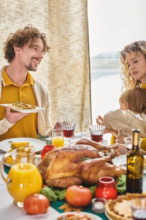 padres felices celebrando el Día de Acción de Gracias con su hija pequeña, un hombre rizado y una mujer cenando