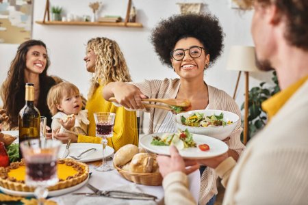 glücklich afrikanisch-amerikanische Frau serviert Salat zu lockigem Mann am Thanksgiving-Tag, lgbt Familie und Baby