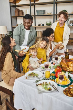 Feliz Día de Acción de Gracias, alegres amigos multiétnicos y reunión familiar en la mesa festiva con pavo