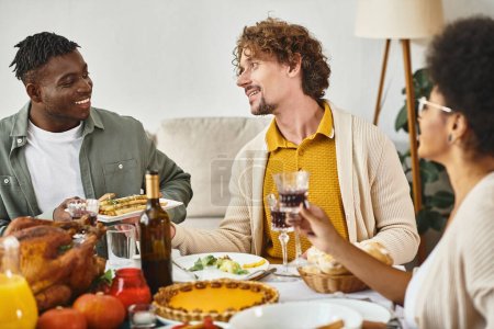 Frohes Thanksgiving, fröhliche multiethnische Freunde plaudern am Tisch mit Truthahn und Kürbiskuchen