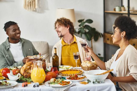 tradición de Acción de Gracias, alegres amigos multiétnicos charlando en la mesa de banquetes con pavo asado