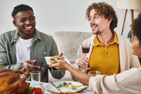 tradición de acción de gracias, hombre americano africano alegre pasando comida a la hermana cerca de amigo feliz