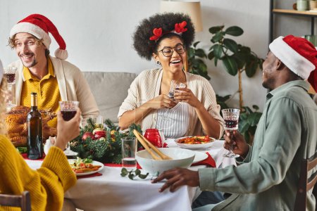 big multicultural family talking and smiling cheerfully at Christmas table wearing Santa hats