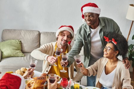 Foto de Gran familia multiétnica sentado y tintineando sus copas de vino en la mesa de vacaciones, Navidad - Imagen libre de derechos