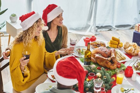 joyful lgbt couple sitting at Christmas table along with their multiethnic family talking cheerfully