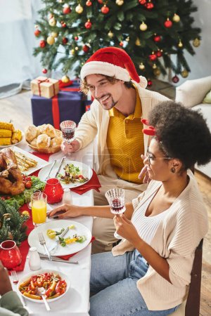 multiethnic family having lively conversation at festive table with Christmas tree on background