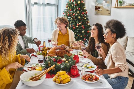 big multicultural family having festive lunch and talking lively with Christmas tree on background