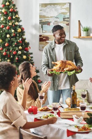 big multicultural family gesturing and laughing and one holding plate with turkey, Christmas