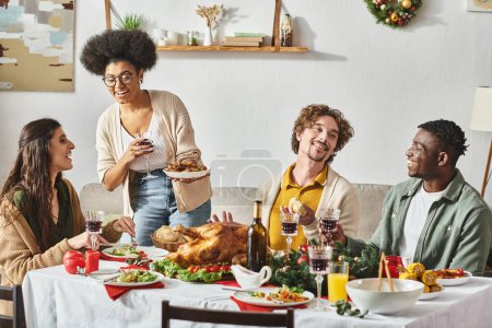 big multicultural family sitting at Christmas table enjoying wine and turkey talking to each other