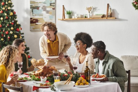 familia multirracial alegre que se divierte mucho en el almuerzo festivo beber vino y comer pavo, Navidad