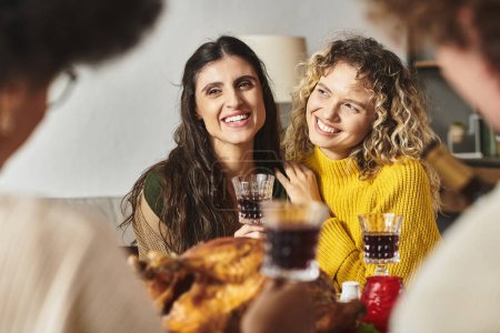 Photo for Joyful lgbt couple surrounded by their family hugging smiling and drinking wine, Christmas - Royalty Free Image