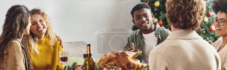 Téléchargez les photos : Jeune famille multiraciale réunie à la table de vacances riant boire du vin, Noël, bannière - en image libre de droit