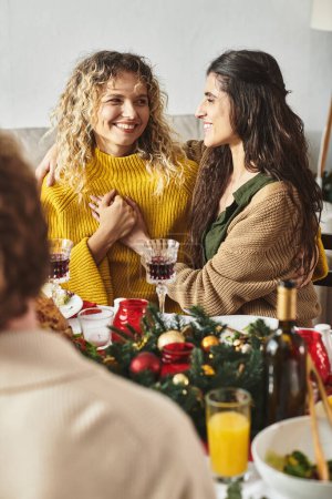 Téléchargez les photos : Doux couple lgbt tenant la main et regardant joyeusement l'autre assis à la table de Noël - en image libre de droit