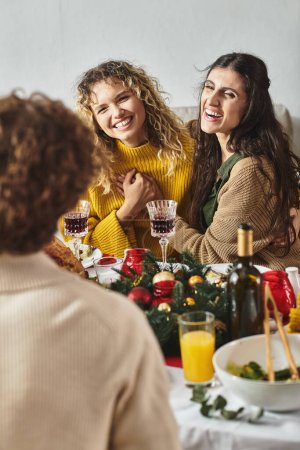 loving lgbt couple sitting at festive table and laughing sincerely holding hands, Christmas