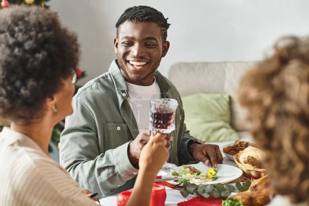 fröhlicher afrikanisch-amerikanischer Mann sitzt an festlichem Tisch, umgeben von seinen Verwandten, Weihnachten