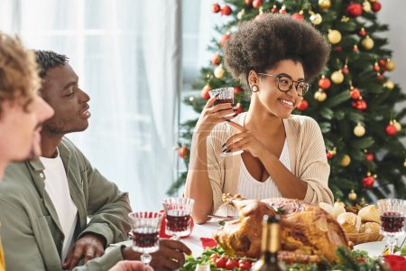 familiares multiculturales disfrutando del vino y la comida en la mesa de vacaciones sonriendo alegremente, Navidad
