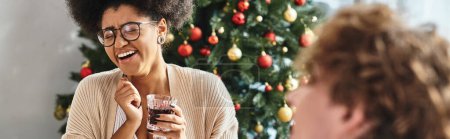 joven jolly africana americana mujer sosteniendo copa de vino y riendo sinceramente, Navidad, bandera