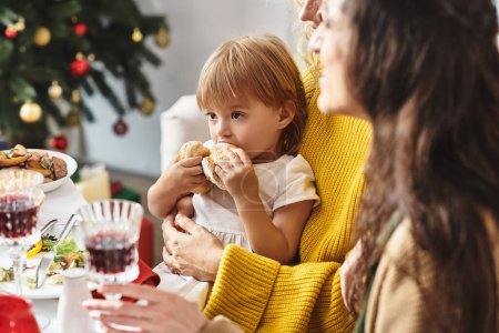 cute little girl sitting at festive table in her parent's hands and looking away, Christmas