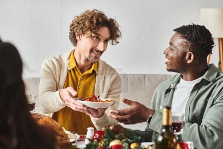 jeunes parents multiculturels assis à la table de vacances et partageant la nourriture entre eux, Noël