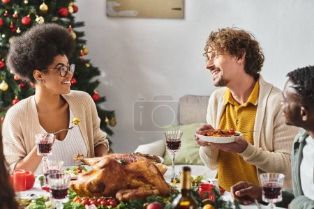 miembros de la familia multicultural felices hablando y mirándose en el almuerzo festivo, Navidad