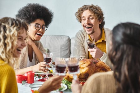 miembros de la familia multicultural feliz riendo en la mesa festiva y tintineo copas de vino, Navidad