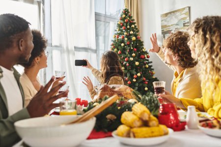 große multikulturelle Familie gestikuliert und macht Selfie am Weihnachtstisch mit Wein und Essen, Weihnachten