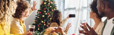 Téléchargez les photos : Grande famille multiculturelle geste agitant et prenant selfie à la table de vacances, Noël, bannière - en image libre de droit