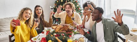 joyful multiracial family taking selfies at holiday lunch with Christmas tree on backdrop, banner