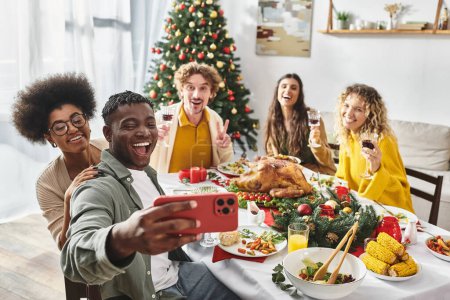 fröhliche multikulturelle Verwandte machen Selfies, trinken Wein und gestikulieren aktiv, Weihnachten