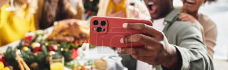 vista recortada de la familia multiétnica tomando selfie en la mesa festiva, fondo borroso, pancarta