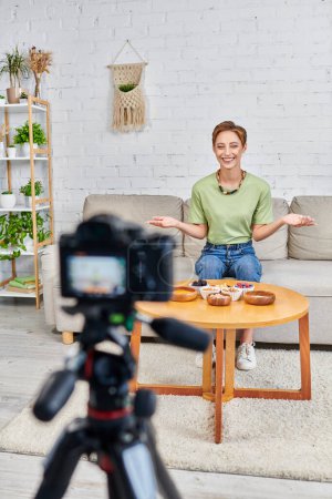 glückliche Frau präsentiert vegetarische Produkte in der Nähe verschwommene Digitalkamera, pflanzliche Ernährung Videoblog