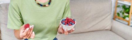cropped view of female vegetarian with blueberries and raspberries in living room, horizontal banner