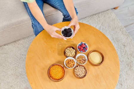 cropped view of woman with fresh blackberries near set of vegetarian products on table at home