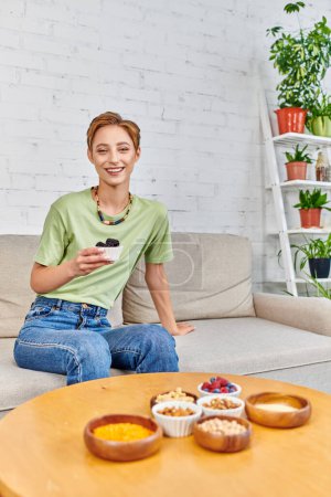 cheerful woman with ripe blackberries near assortment of plant-based food on table in living room