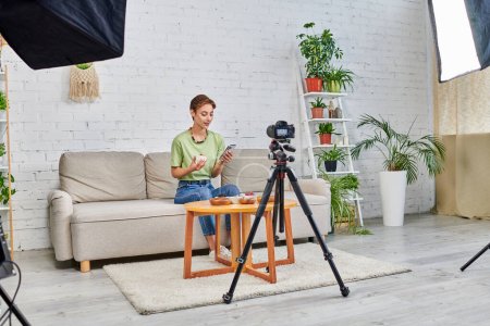 Téléchargez les photos : Blogueur vidéo avec smartphone près de la nourriture végétarienne et appareil photo numérique avec lampe softbox à la maison - en image libre de droit