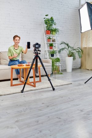 vegetarian woman holding smartphone with blank screen during video blog on plant-based diets at home