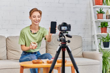 Téléchargez les photos : Heureuse femme végétarienne tenant smartphone avec écran blanc pendant blog vidéo sur les régimes à base de plantes - en image libre de droit