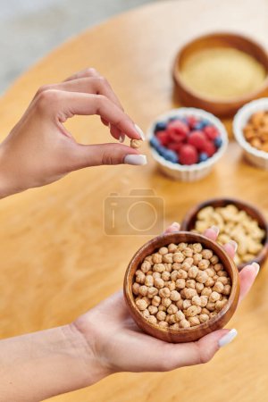 cropped view of woman with bowl of chickpeas above various vegetarian products on blurred table