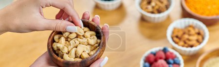 partial view of woman with bowl of cashews above various plant-based food on blurred table, banner