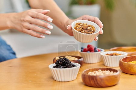partial view of woman with bowl of walnuts near blackberries and assortment of plant-based food