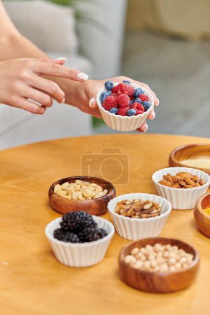cropped woman pointing at bowl with fresh strawberries and blueberries near various vegetarian food
