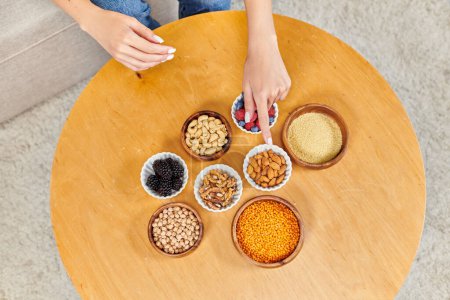 Téléchargez les photos : Femme cultivée pointant vers la table avec diverses baies et noix avec des légumineuses, nutrition à base de plantes - en image libre de droit
