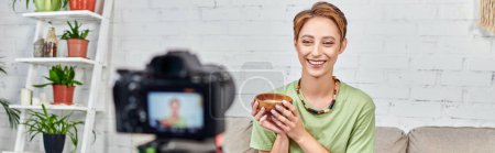 Photo for Cheerful female video blogger holding bowl with vegetarian food near blurred digital camera, banner - Royalty Free Image