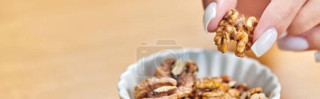 cropped view of woman taking walnut from white ceramic bowl, vegetarian concept, horizontal banner