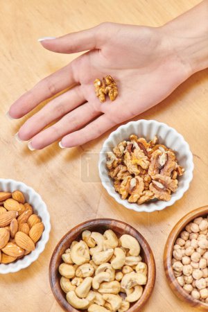 top view of female hand with walnut near almonds and cashews with chickpeas in bowls, vegetarianism