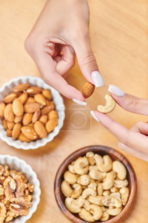 cropped view of woman holding cashew and walnut above bowls with nuts, high calorie plant-based food