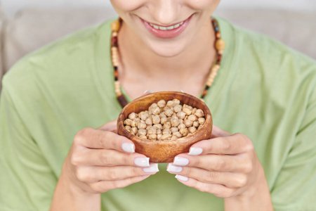 cropped view of happy vegetarian woman with wooden bowl of chickpeas, nutritious vegetarian diet