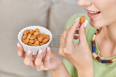partial view of young woman with white ceramic bowl of almonds, delicious vegetarian diet concept