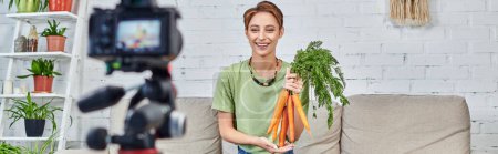 happy vegetarian woman with fresh carrots near blurred digital camera, vegetarian video blog, banner