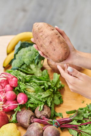 Photo for Female hands with sweet potato above fresh radish and beetroots near fruits, healthy vegetarian diet - Royalty Free Image